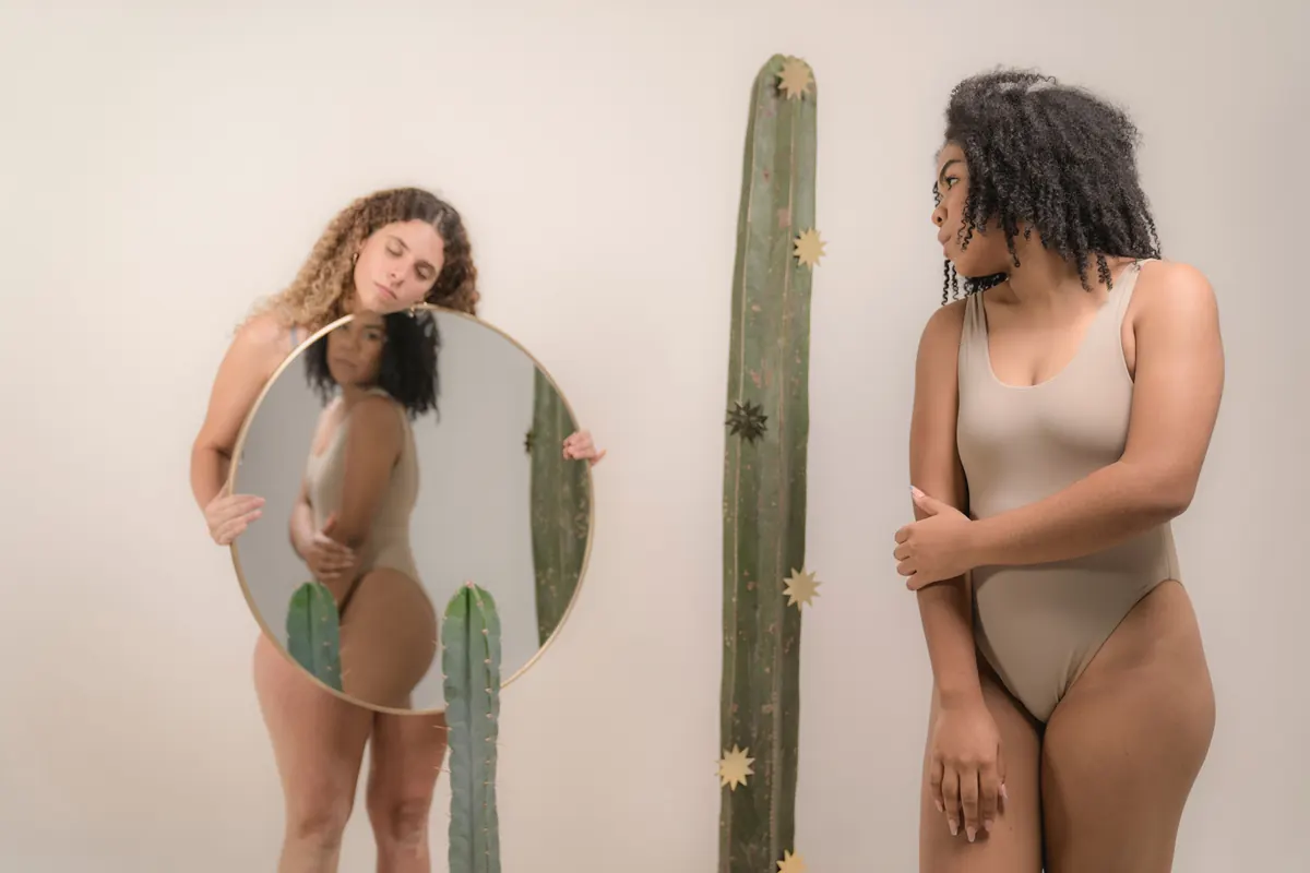 Dos mujeres frente a un espejo redondo, mirándose sin prisa